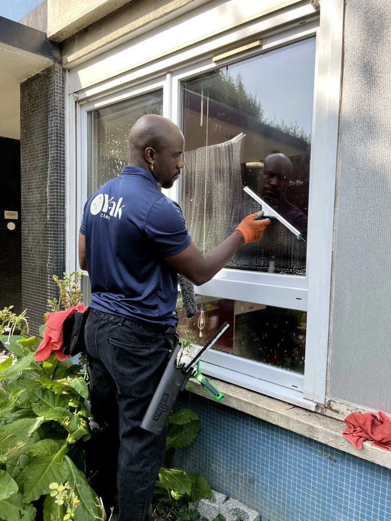 May, technicien chez Yak Clean qui nettoie une vitre à l'aide d'une raclette